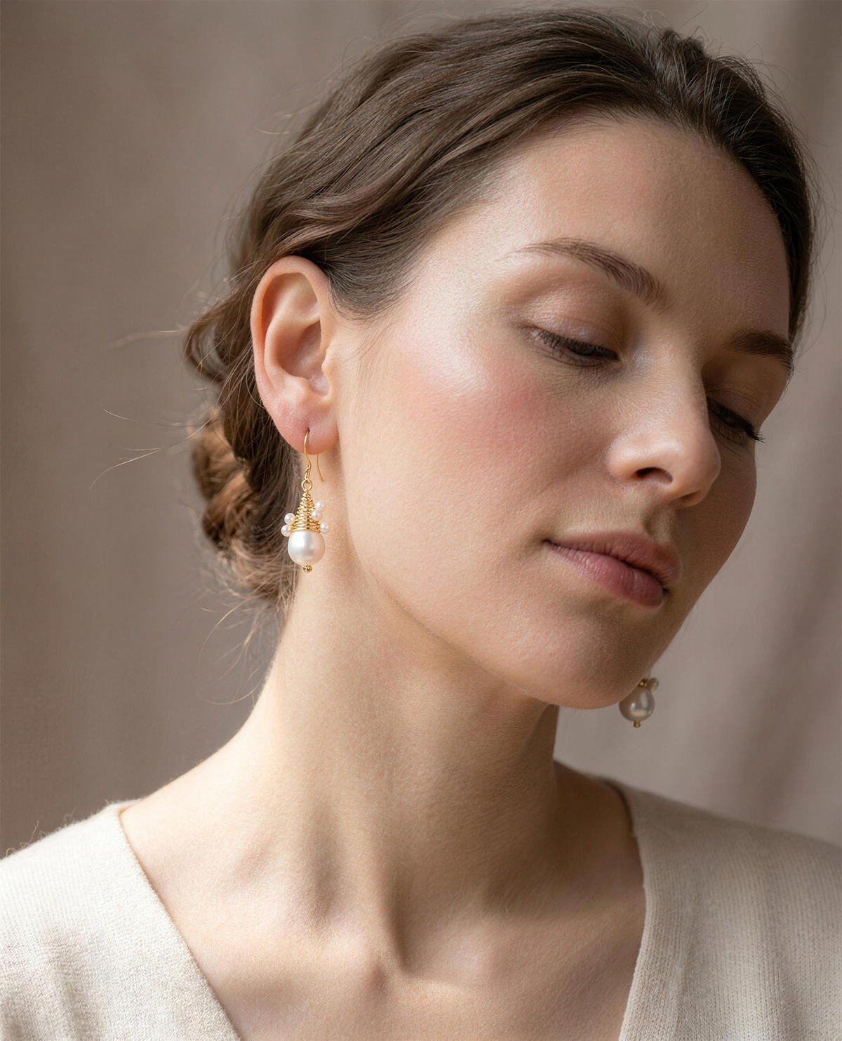 Wire-wrapped freshwater pearl drop earrings worn on the ear, head tilted.