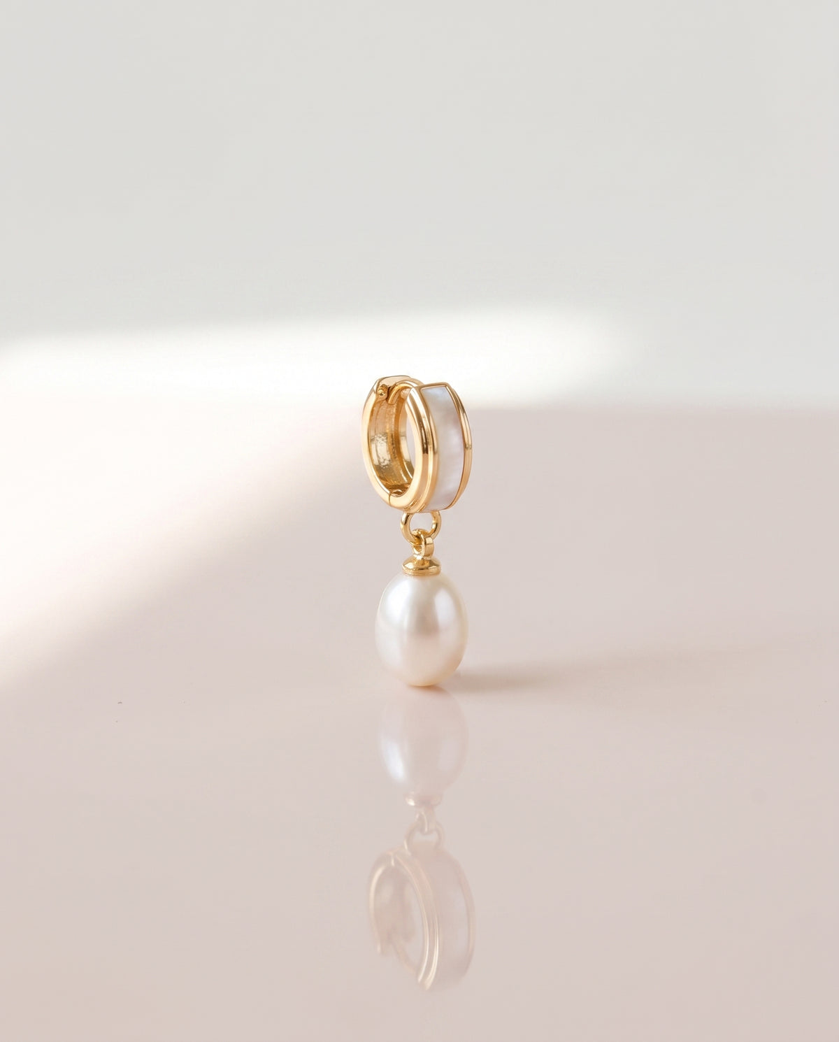 Shell Inlay Pearl Huggie Drops freshwater pearl earring on a glossy pedestal with soft reflection