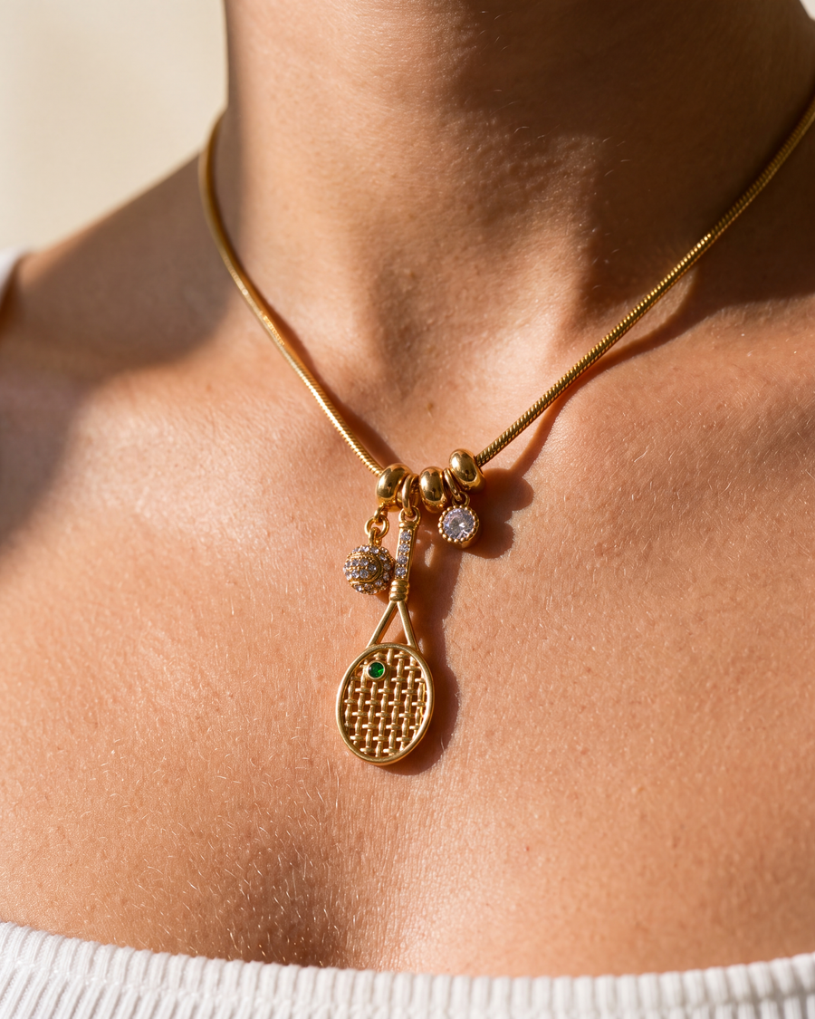 Close up of the tennis racquet charm showing the woven gold strings and green stone
