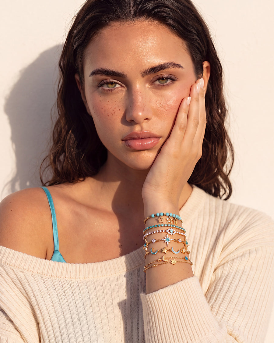 Model wearing the star and moon bracelet stack, hand resting against her cheek