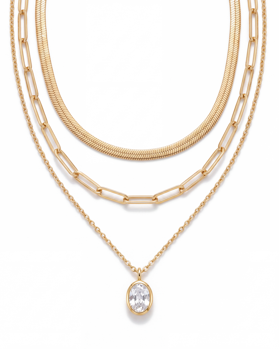 Three gold chains laid out on a white background with the oval crystal pendant