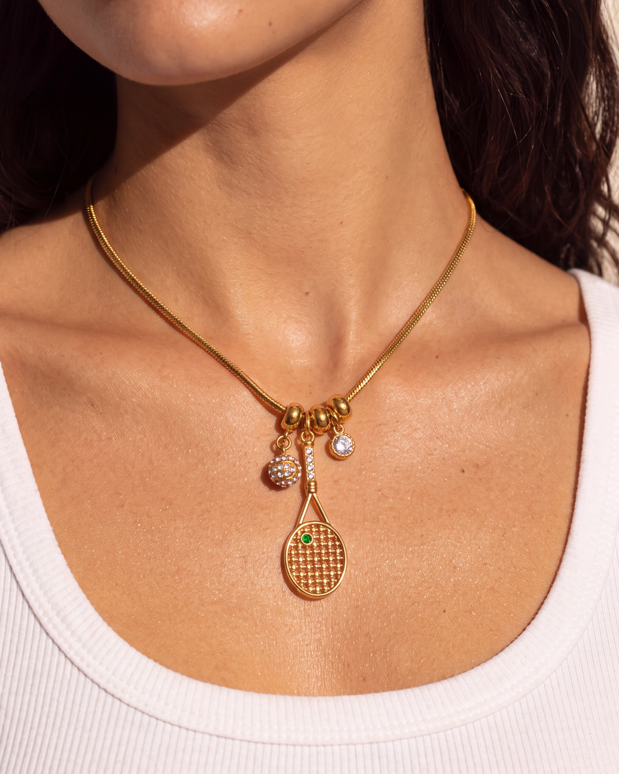 Gold tennis charm necklace sitting just below the collarbone notch
