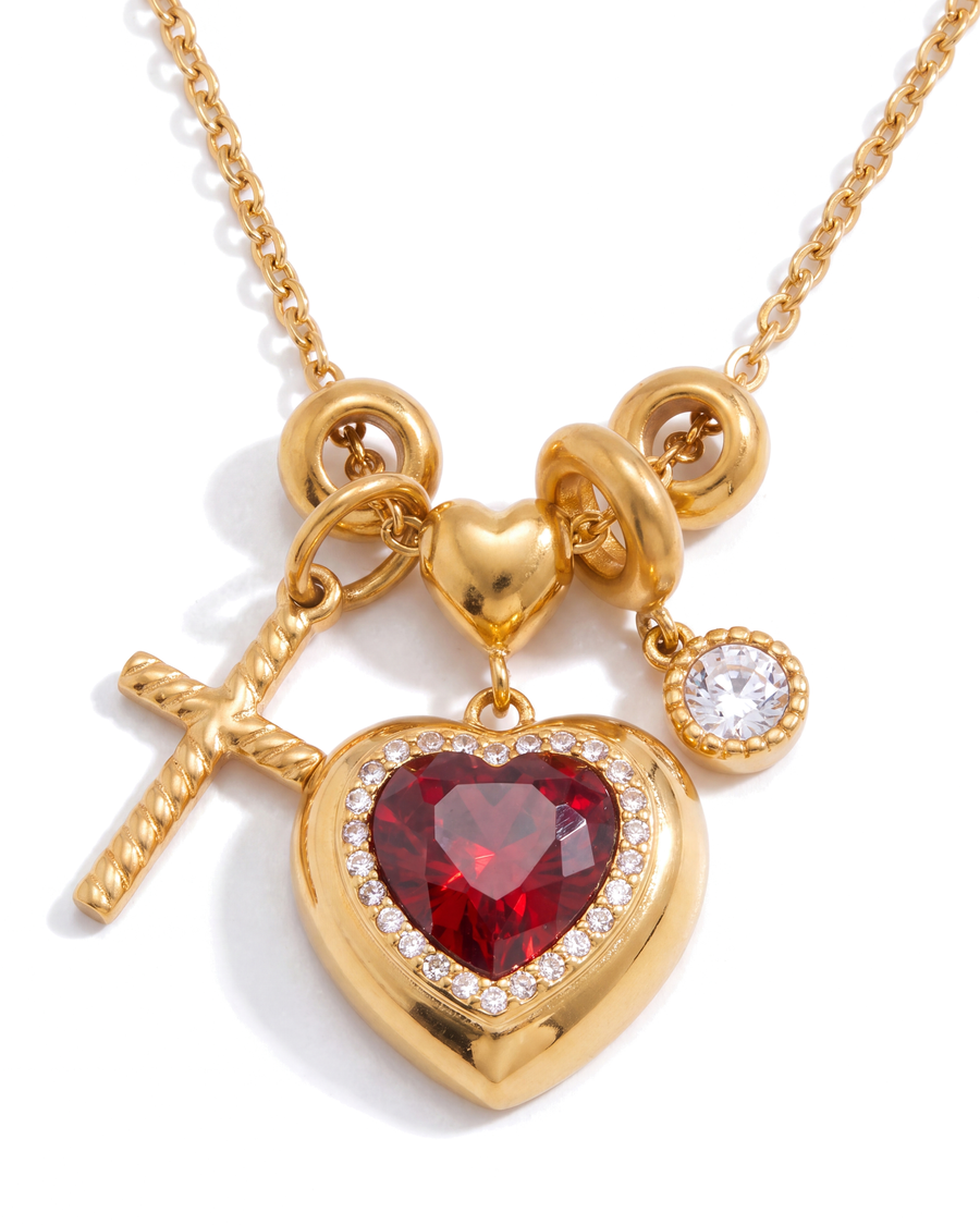 Close view of the charm cluster - puffed gold heart with a red stone, rope cross, clear stone and two open rings
