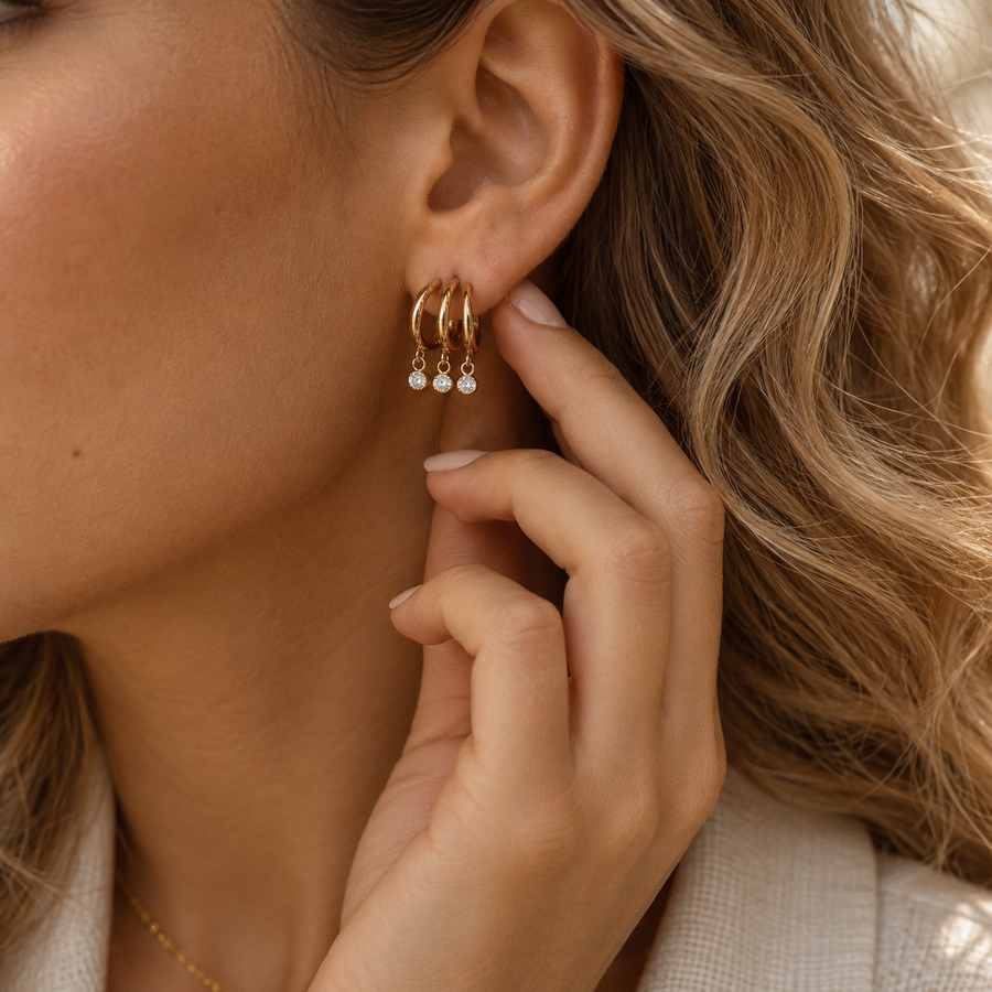 Triple hoop crystal drop earrings worn on the ear, three nested gold hoops each with a bezel-set crystal drop, on a single post