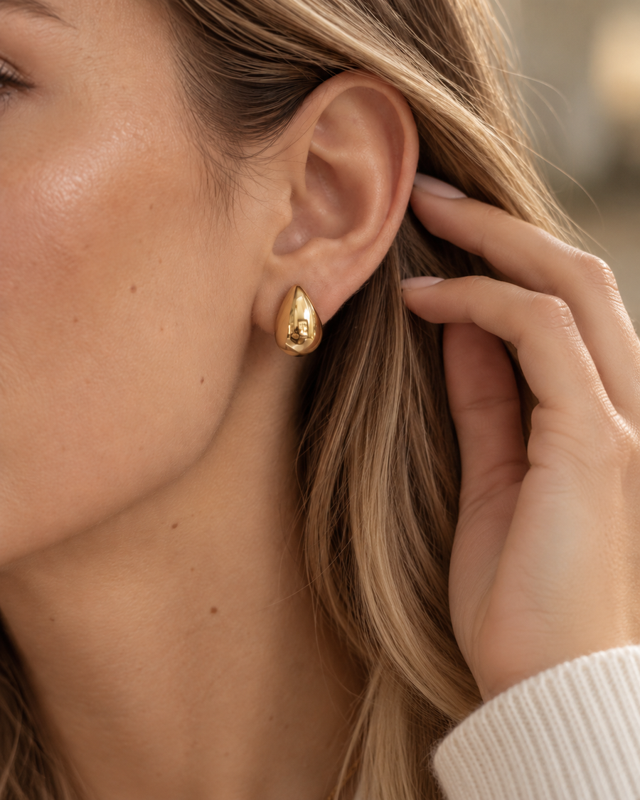 Teardrop huggie earring on the ear in natural light, smooth gold teardrop with no seam or stone, 18k gold plated stainless steel