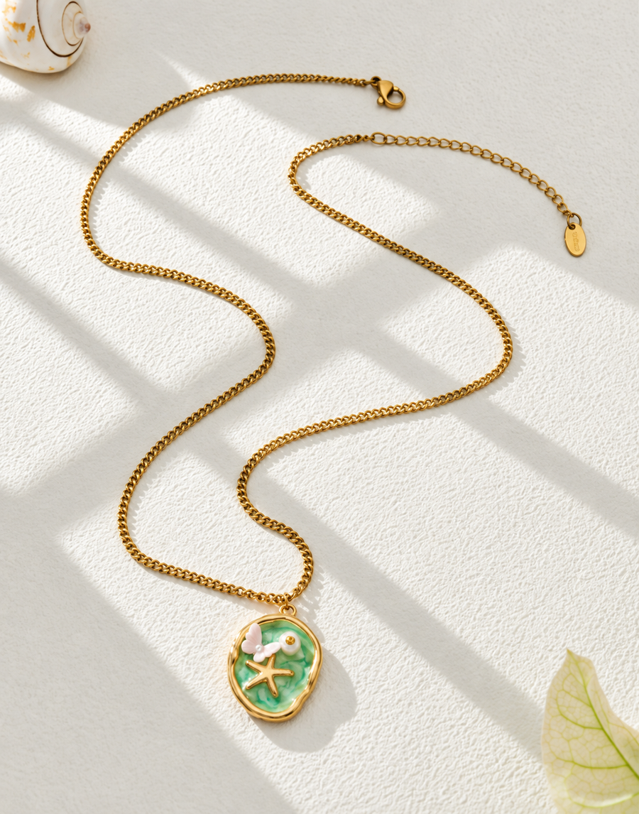 Painted miniature pendant necklace laid in sunlight beside a leaf, chain and clasp visible