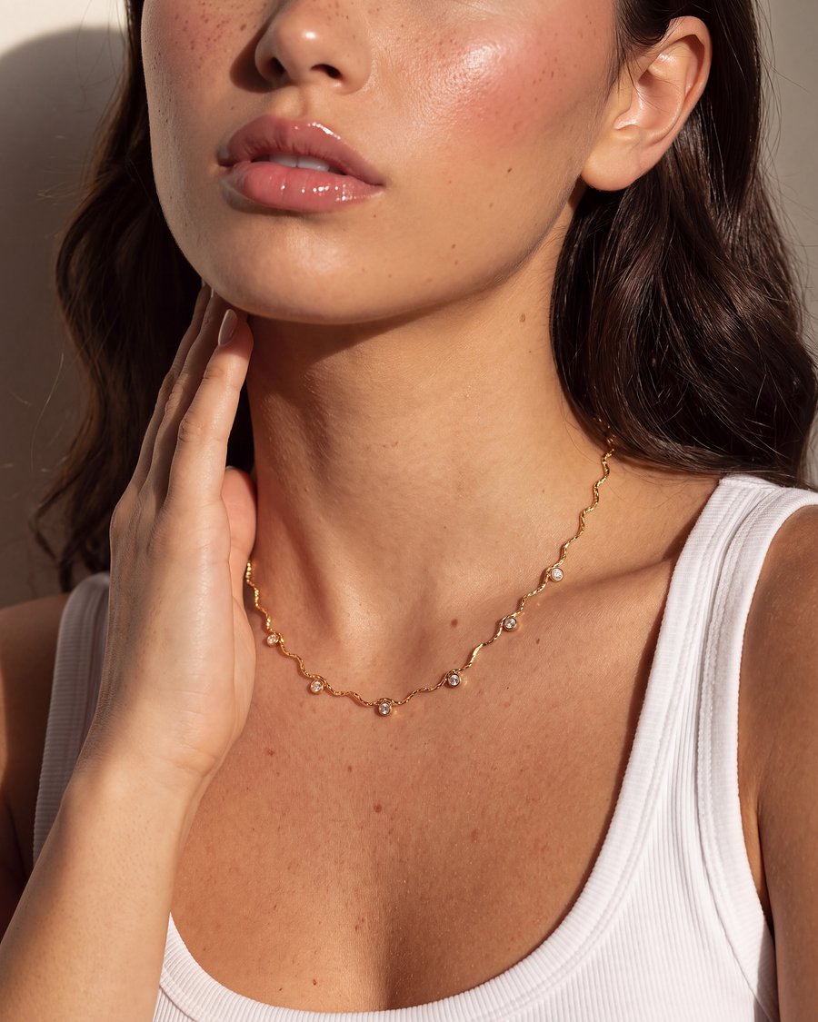 Model with a hand at her jaw, the gold wave chain necklace across her collarbones