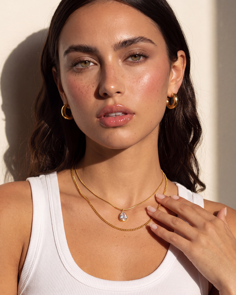 Hand resting at the collarbone beside the layered gold chains