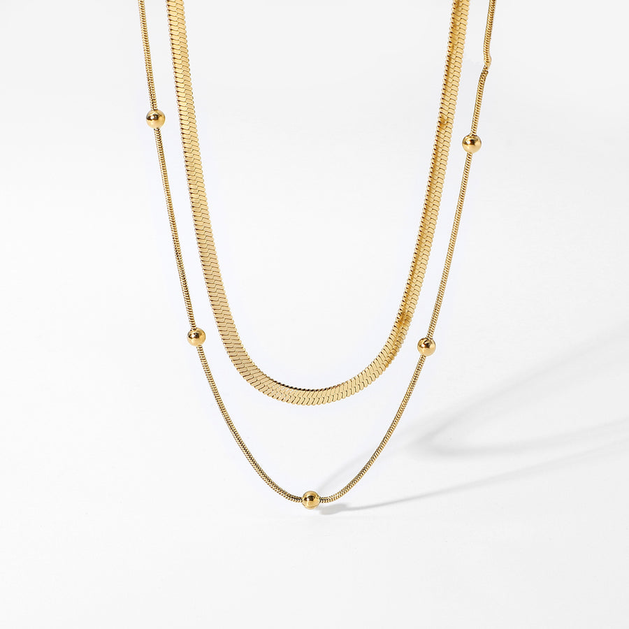 Herringbone gold chain and finer beaded chain necklace set laid flat on a white background