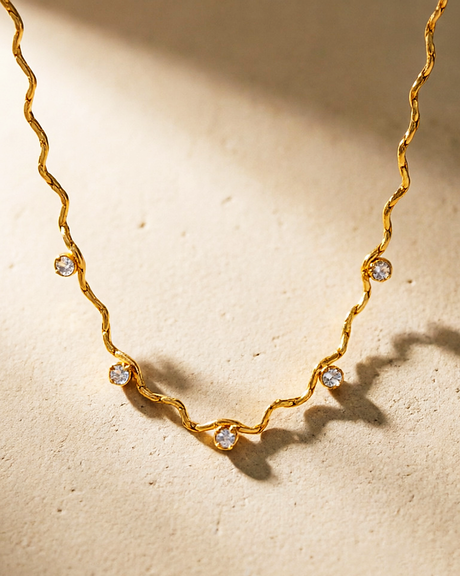 The gold wave chain necklace in raking sunlight, showing its mirror polish
