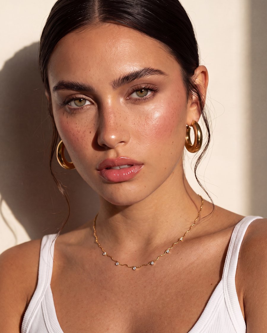 Model wearing the gold wave chain necklace at the base of the throat with a white tank