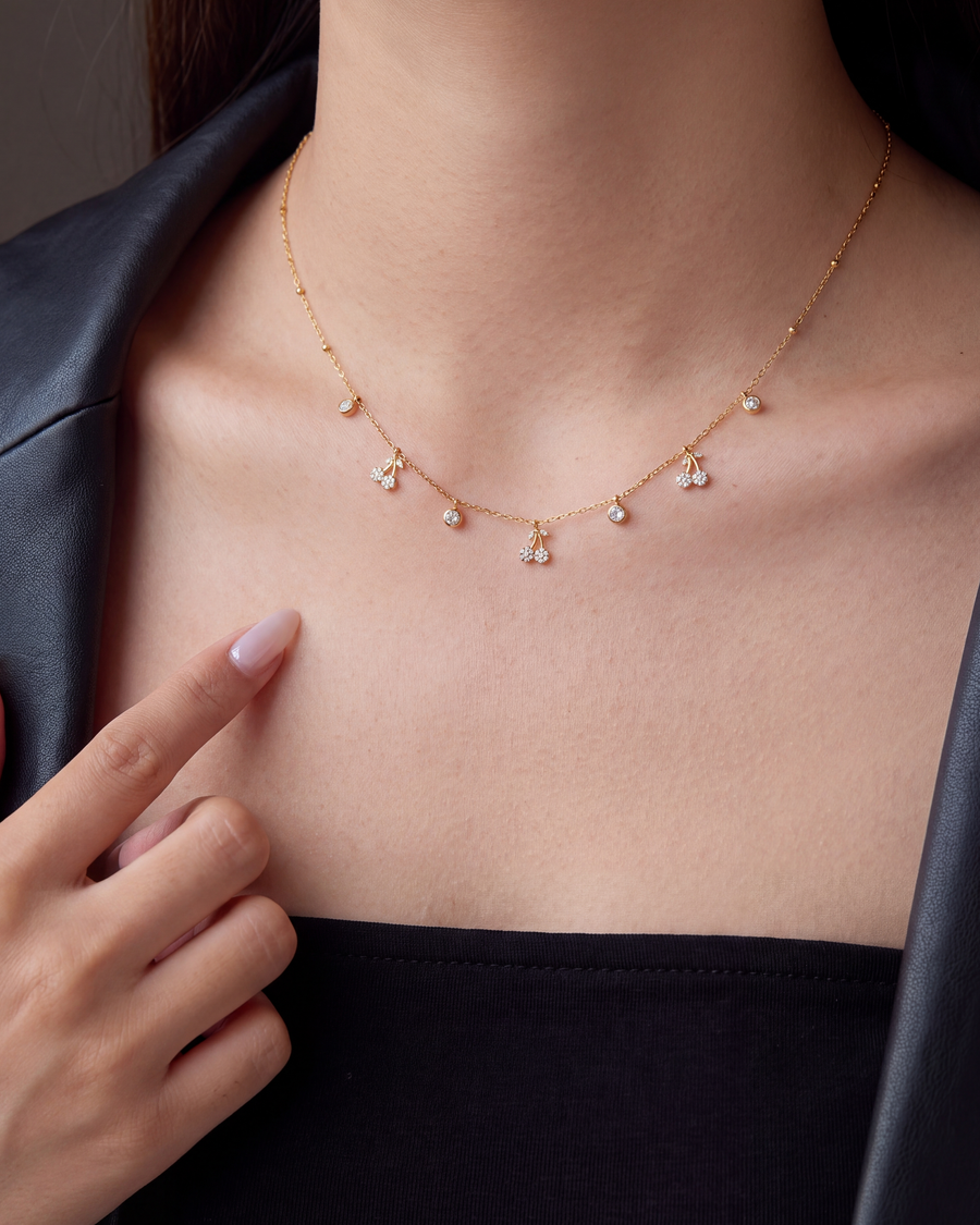 A fingertip resting against the fine chain beside a cherry charm