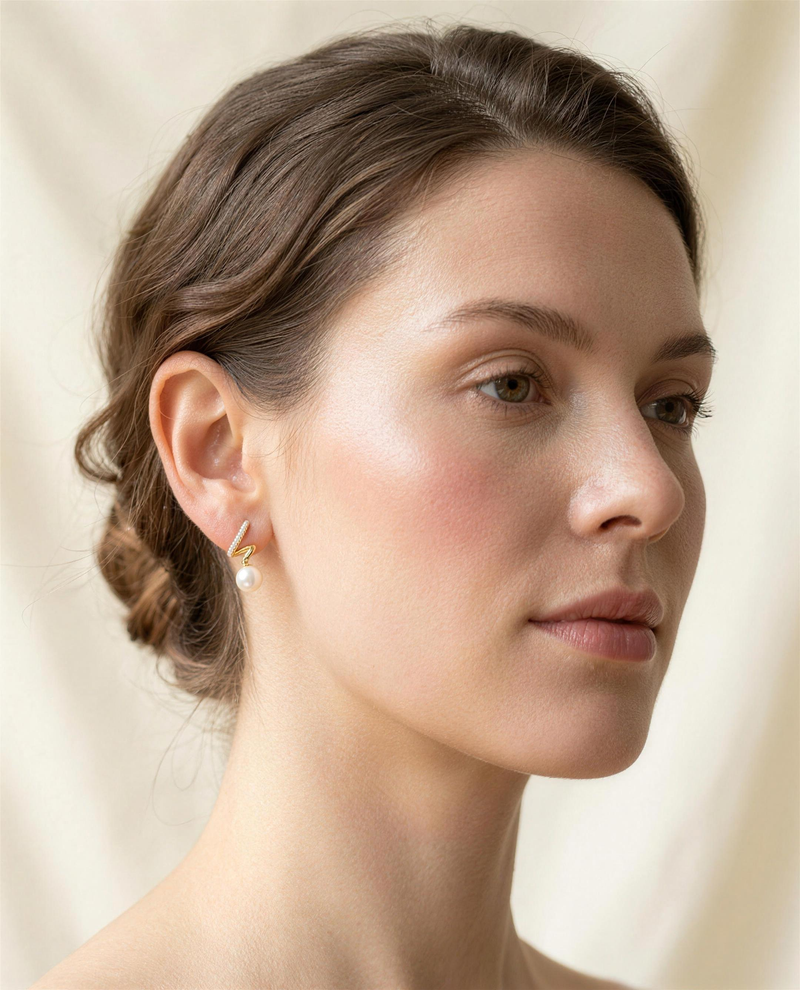 Gold spiral freshwater pearl stud earrings worn on the ear, side profile.