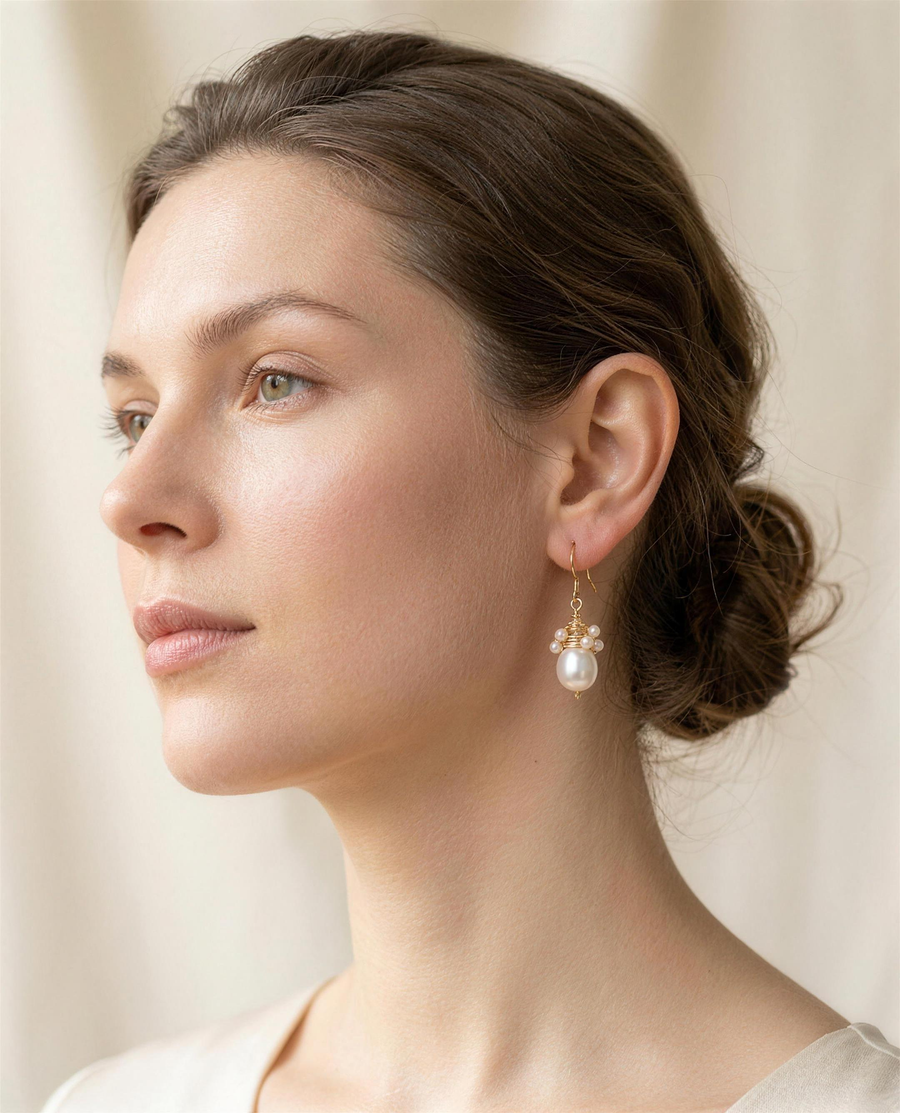 Wire-wrapped freshwater pearl drop earrings worn on the ear, three-quarter view.