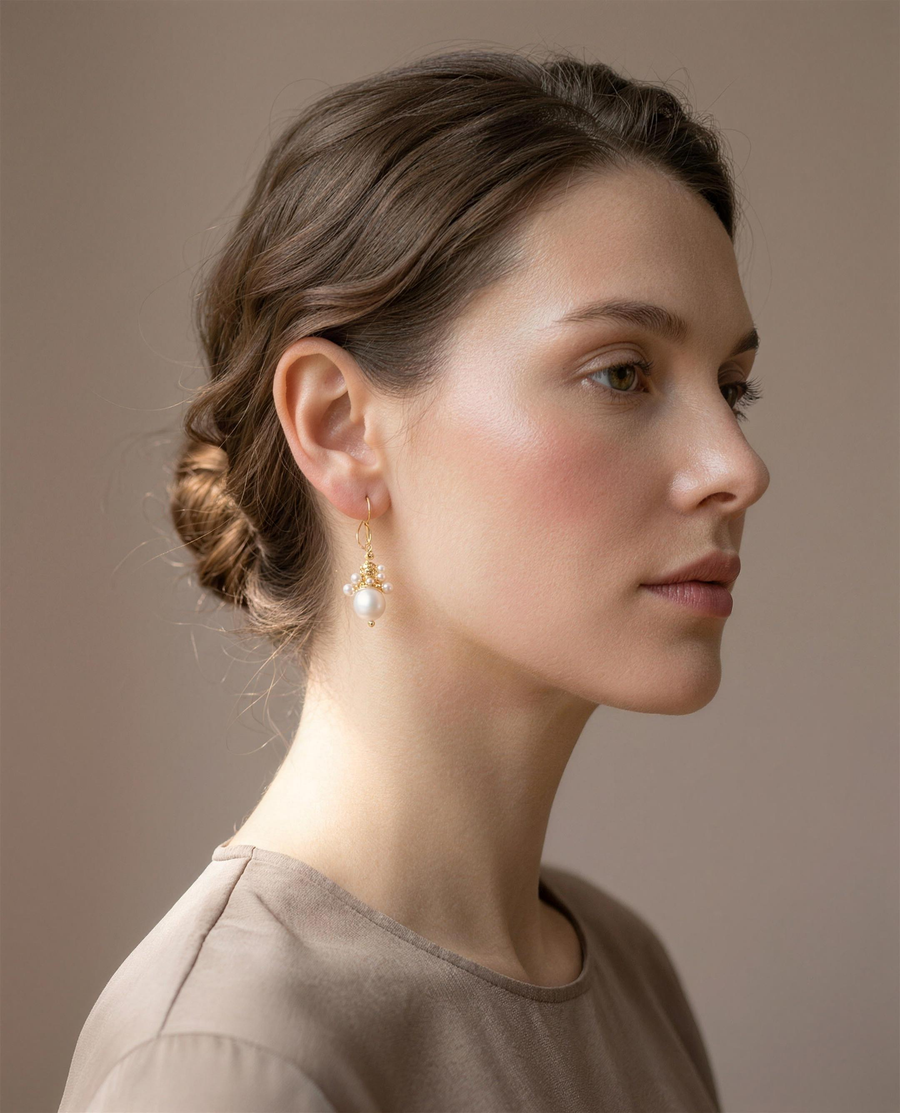 Wire-wrapped freshwater pearl drop earrings worn on the ear, side view.