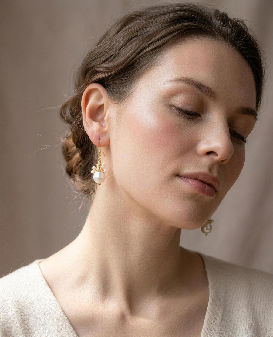 Wire-wrapped freshwater pearl drop earrings worn on the ear, head tilted.