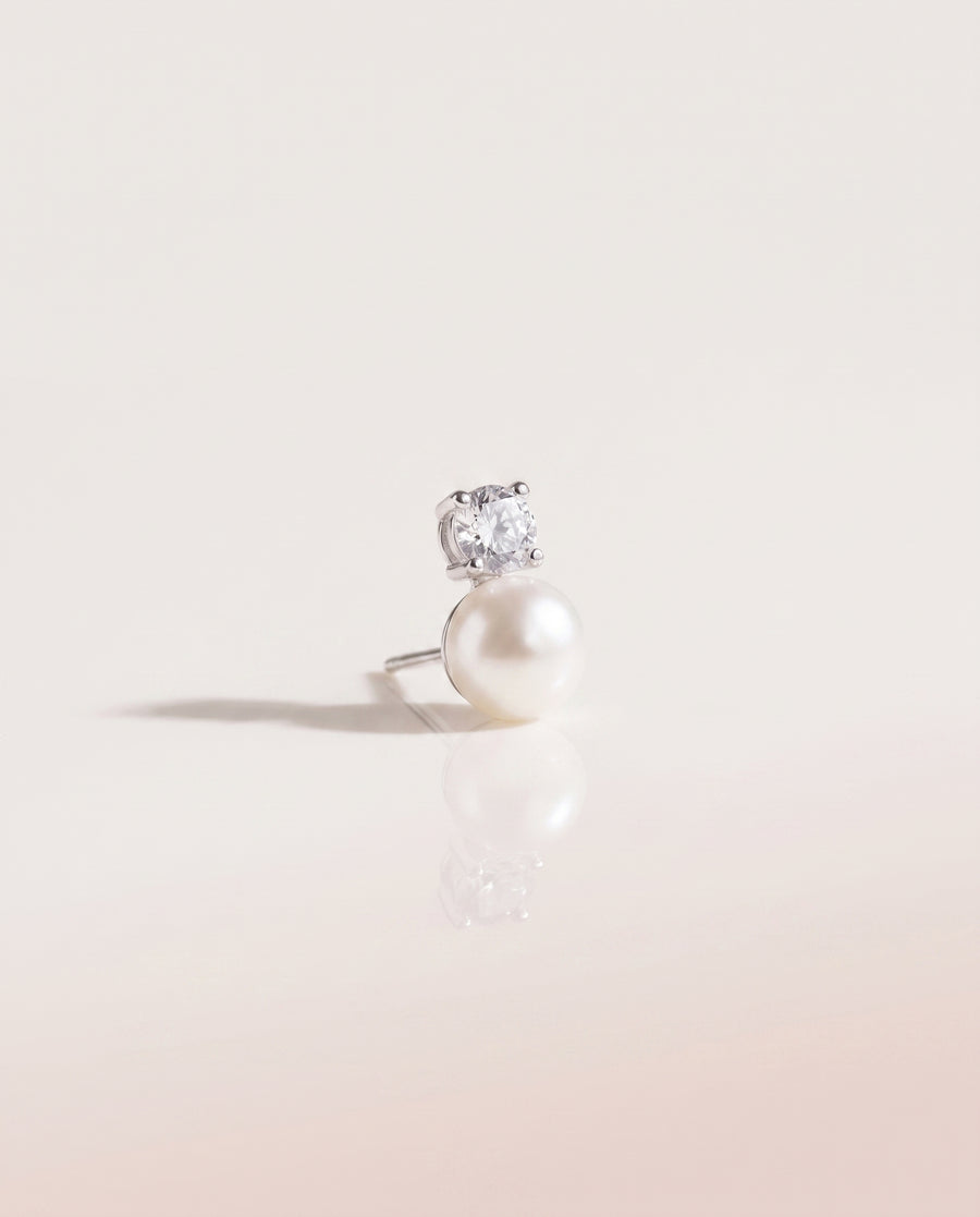 Solitaire and Pearl Studs freshwater pearl earring on a glossy pedestal with soft reflection